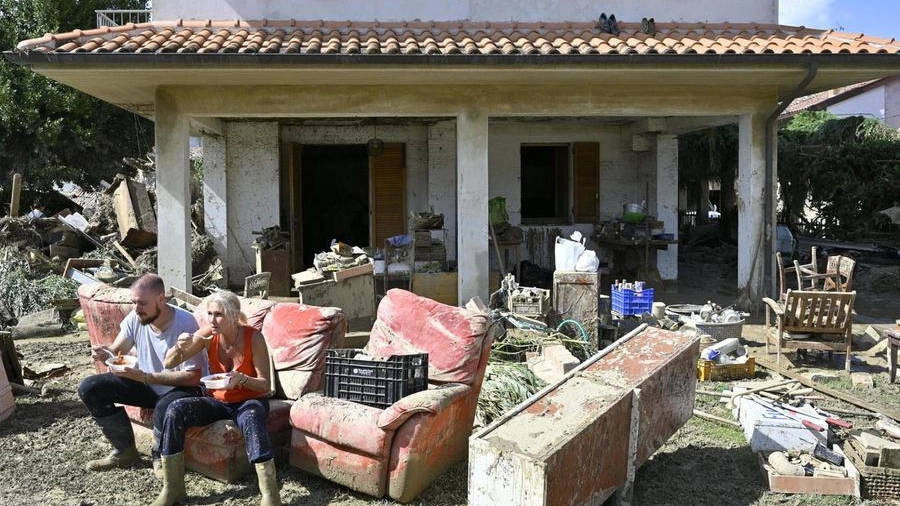 Una coppia mangia sul divano distrutto posizionato in giardino dopo l'alluvione (Ansa)