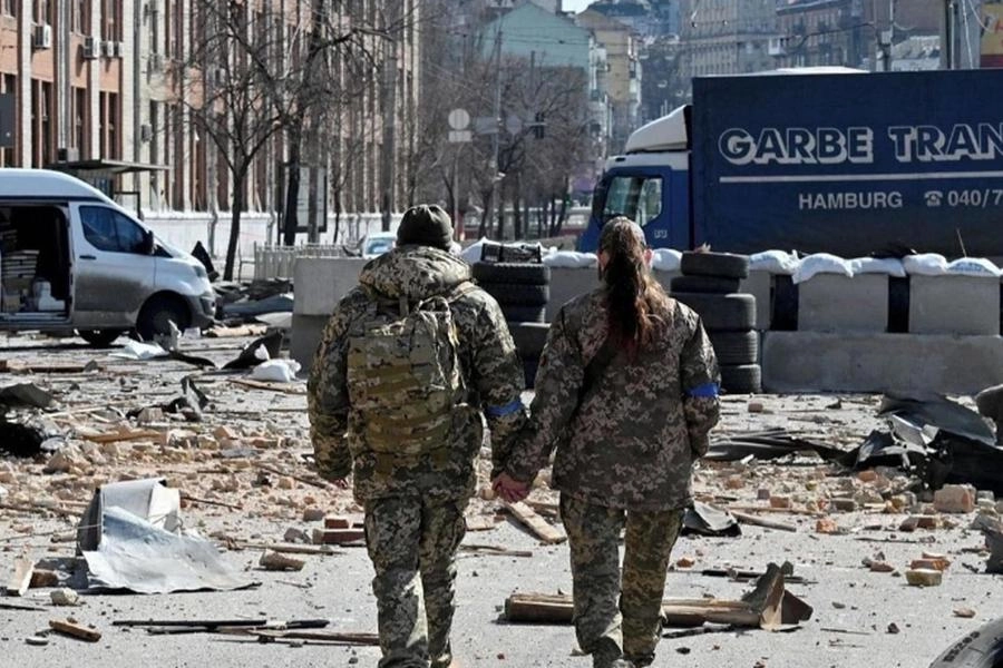 Un soldato e una soldatessa ucraini camminano tra le macerie tenendosi per mano