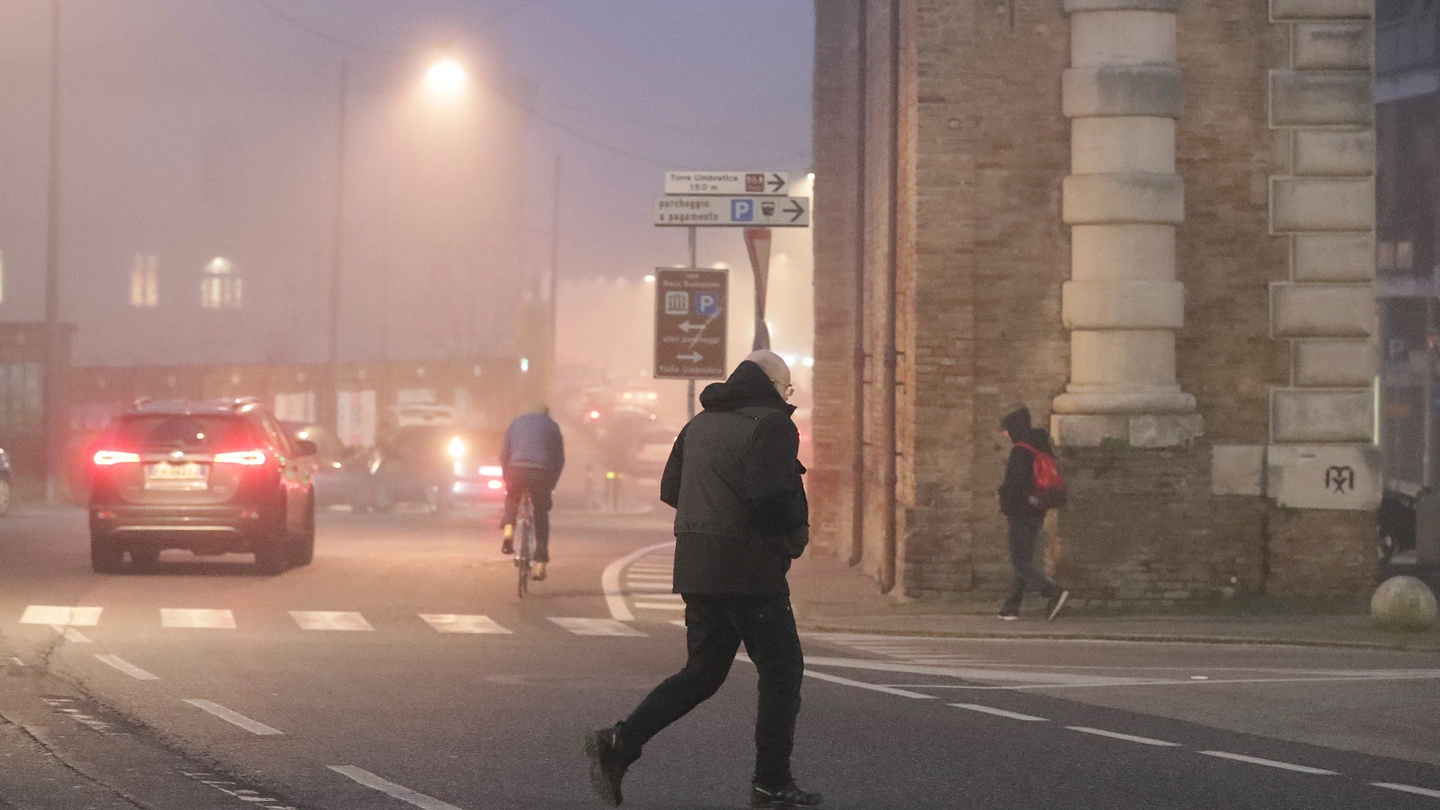Un pedone attraversa fuori dalle strisce pedonali e di sera fra la nebbia in via di Roma