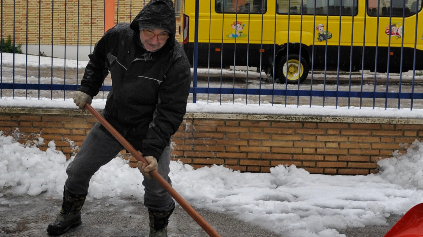 Un uomo spala la neve davanti  alla scuola di Sforzacosta