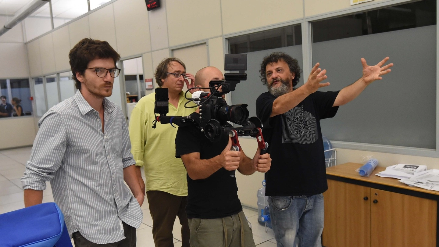  Bob Messini nei panni di un giornalista, si batte un ciak, il regista Marco Manetti al monitor e con gli attori Lorenzo Pedrotti e Messini mentre spiega la scena da girare