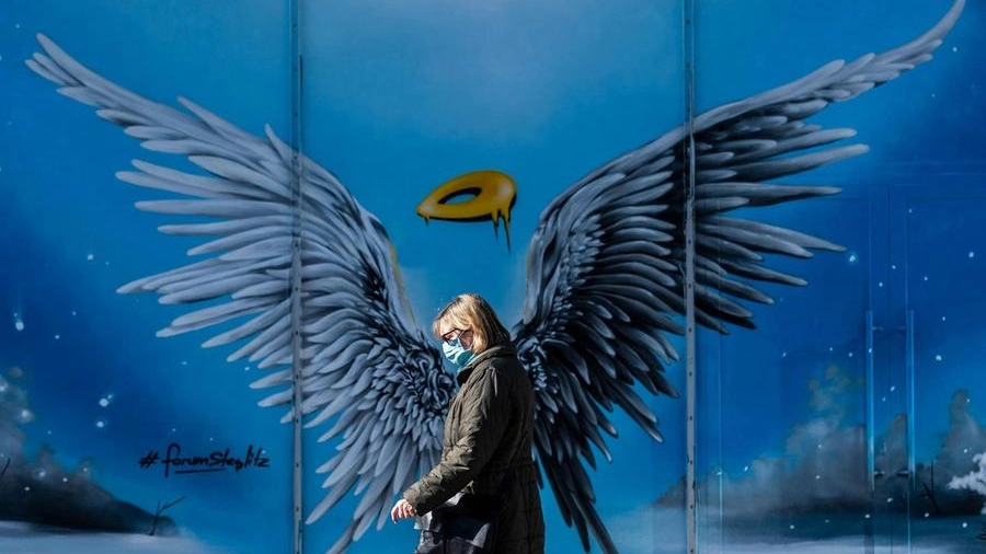 Una donna con la mascherina passa davanti a un murales in Germania (Ansa)