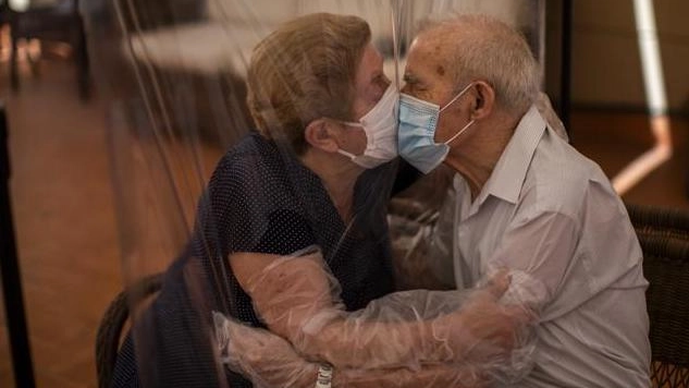 Due anziani si baciano con la mascherina attraverso un telone di plastica in una Rsa