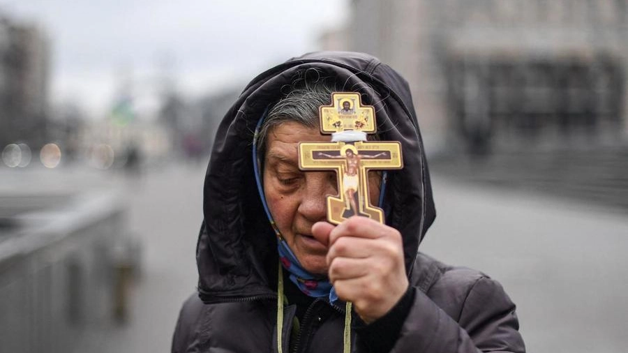 Una donna ucraina espone il crocifisso nelle strade di Kiev bombardate (Ansa)