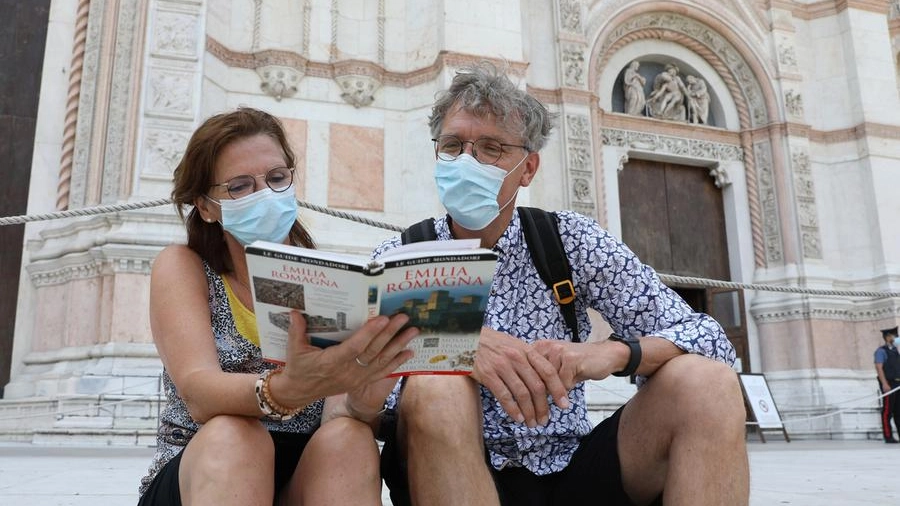 Due turisti consultano la guida dell’Emilia-Romagna sui gradini di San Petronio
