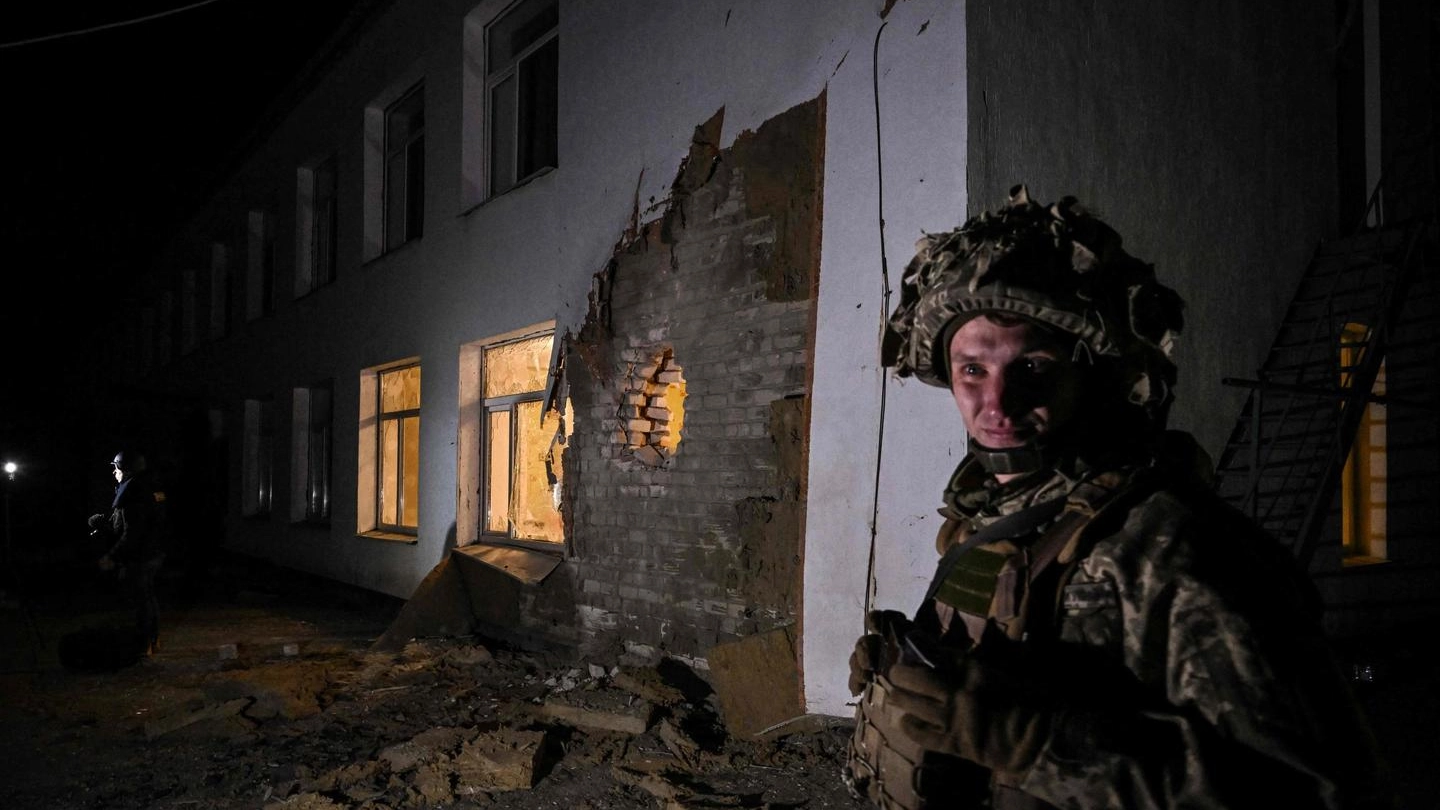 Soldato ucraino accanto all'asilo bombardato (Ansa)