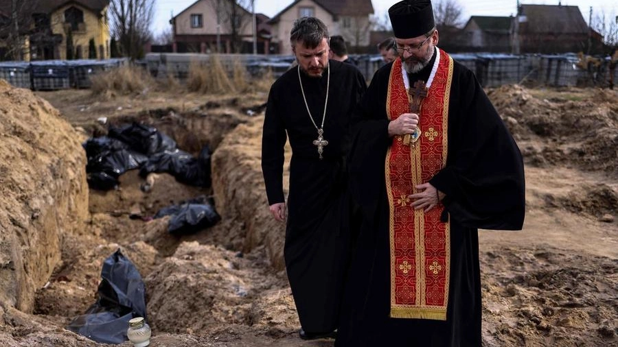 Un prete prega per le vittime trovate delle fosse comuni di Bucha (Ansa)