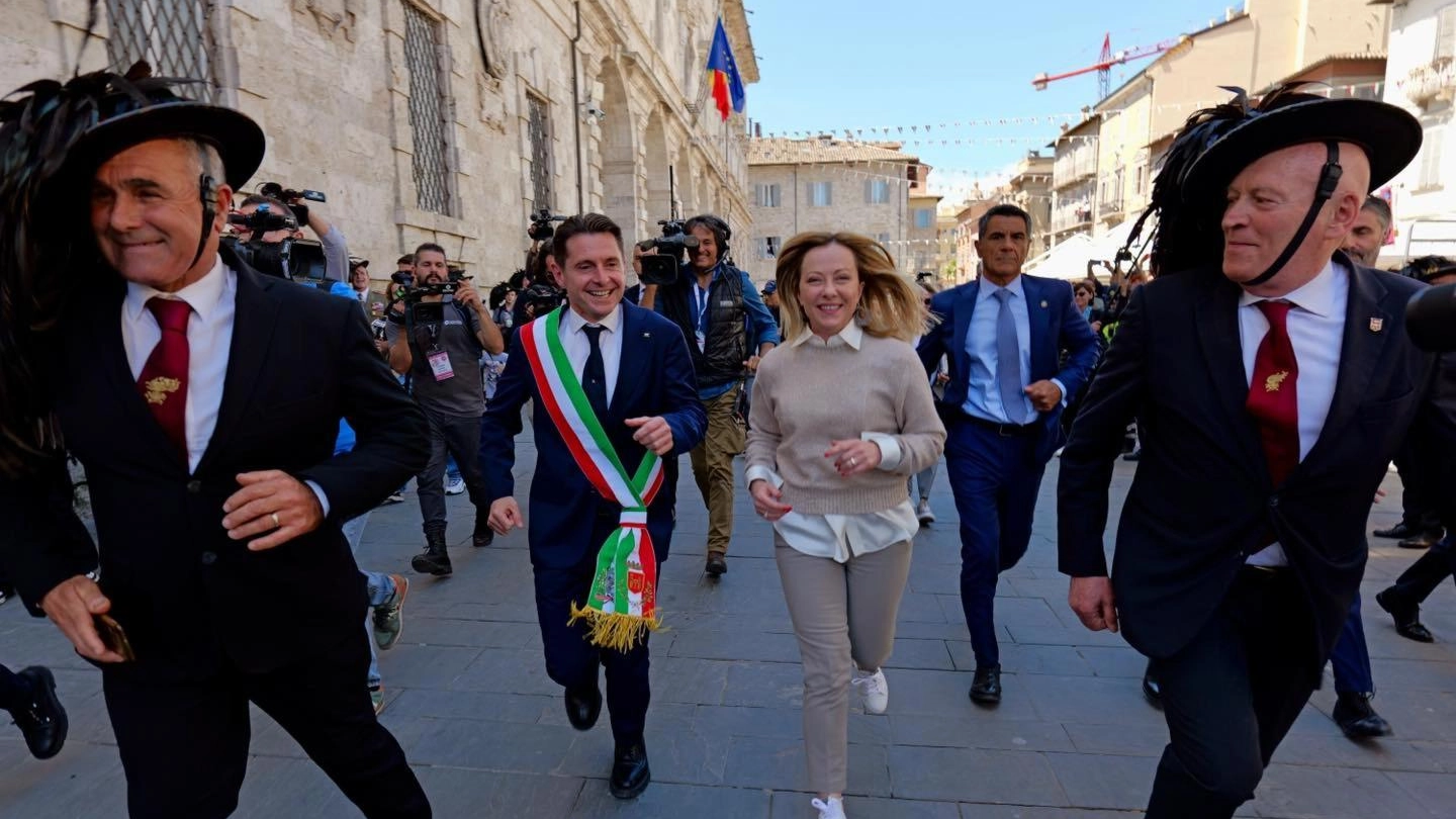 La premier Giorgia Meloni accenna la corsetta del bersagliere e al suo fianco c’è il sindaco di Ascoli, Marco Fioravanti