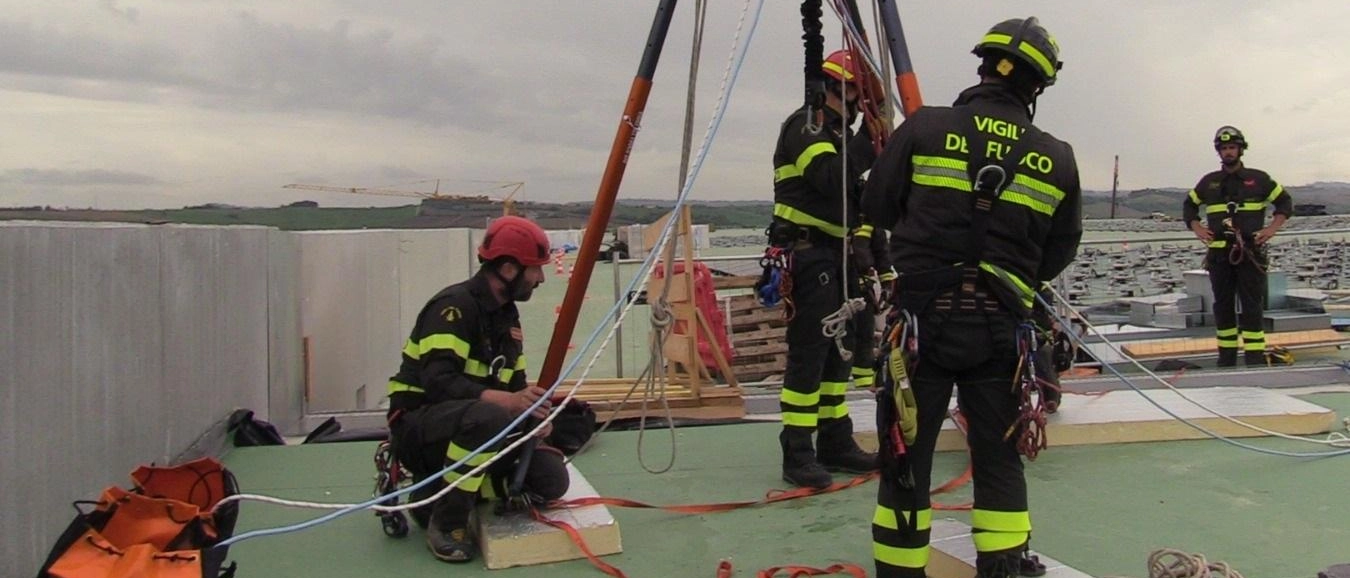 Esercitazione dei vigili del fuoco ad Ancona nel capannone Amazon a Jesi per soccorrere un uomo ferito sul tetto con tecniche innovative e attrezzature speciali.