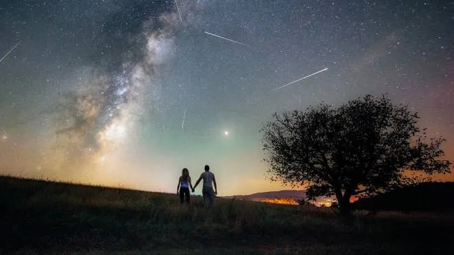 Young man and woman under the bright night sky watching the milky way and Perseid meteor shower
