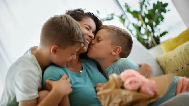 Sons hugging and kissing their mother and giving her a bouquet of roses for Mother's Day.