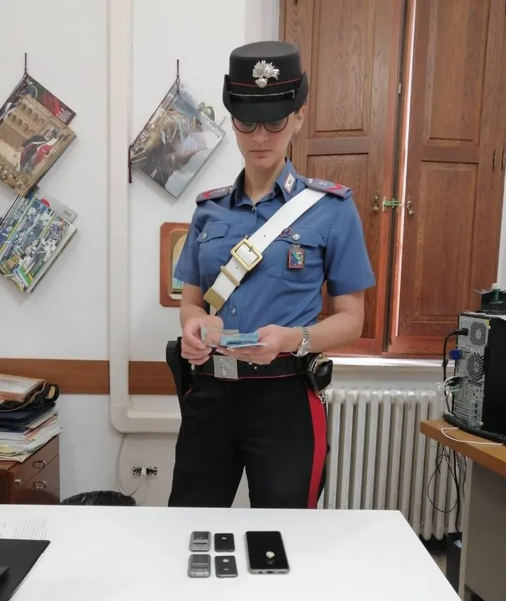 Una carabiniere mostra la droga, i contanti, i cellulari e il bilancino di precisione trovati in casa della giovane