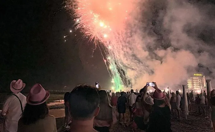 I fuochi d’artificio per la Notte Rosa visti dai turisti sulla spiaggia di Riccione