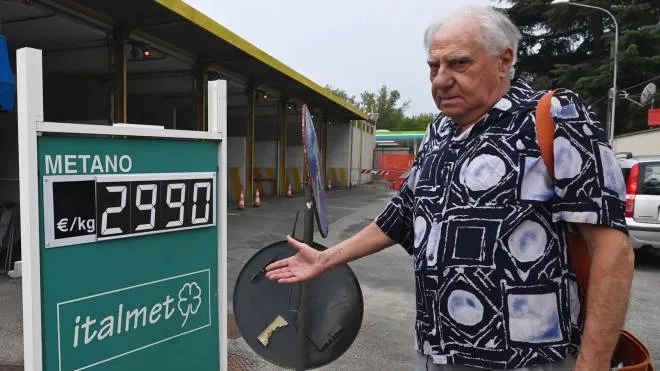 Un automobilista indica sconsolato il cartello con il prezzo del metano al chilogrammo, che è arrivato a sfiorare i tre euro